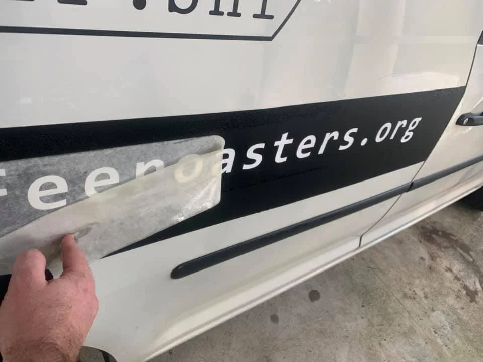 Application tape being removed from vinyl lettering on a white vehicle